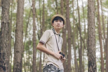 Asia man wears shirt, hat, and camouflage pants are walking and taking photos at the forest.の写真素材
