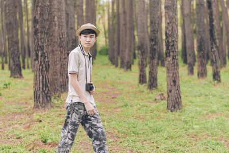 Asia man wears shirt, hat, and camouflage pants are walking and taking photos at the forest.の写真素材