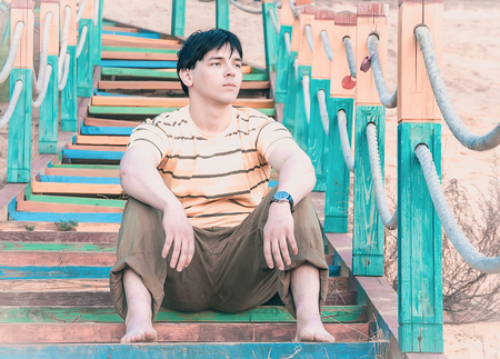 Barefoot young man sitting on colorful stairs on the beachの写真素材