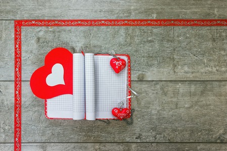 Open notebook with bookmarks and pendants in the form of red and white hearts lying on a wooden tableの写真素材