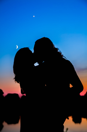 Silhouette of a kissing couple in the night sky with the moon.の写真素材