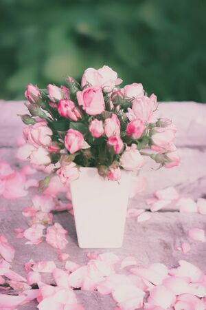 Bouquet of roses in white vase on the table made of planks on a green background. Greeting card. Toned, blurry, vintage filter.の写真素材