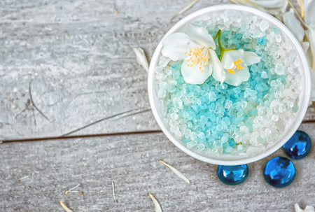Salt for spa treatment with a branch of jasmine and pebbles on a wooden table. Blurring background. Selective focus.の写真素材