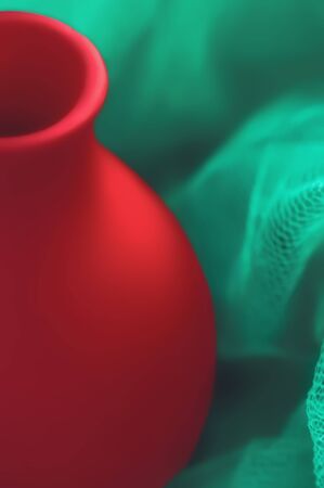 Abstract bicolor design - part of a red ceramic vase on a blurred green background closeup. Selective soft focus.の写真素材