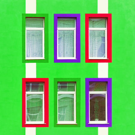 Part of the green wall of the building with colorful red and purple rectangular windows.の写真素材