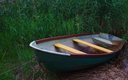 The old blue fishing rowing boat is moored among the reed thickets in a summer evening twilight. Selective focus.の写真素材