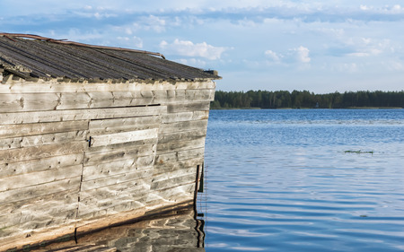 Old wooden boathouse is reflected in the surface of the river under a blue sky on a summer sunny day. Selective focus, space for copy.の写真素材