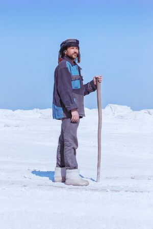 Man with a staff in ethnic clothes standing among mounds of white sand or snow under a blue sky. Gypsum mining. Moscow region, Russia.の写真素材