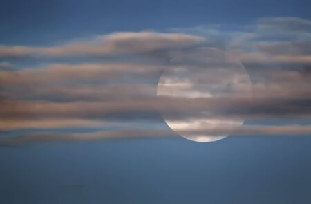 The big full moon in the blue sky behind the clouds out of focus in the early morning. Natural background with space for copy and design.の写真素材