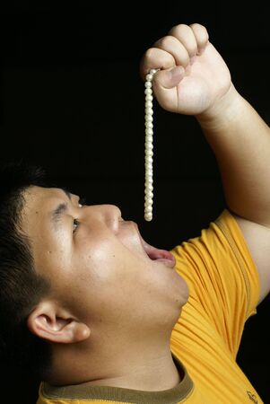 Asian man eating string of pearlsの写真素材
