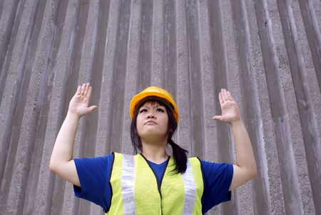 Asian female construction worker with hand signal for stop and urban wall for backdrop