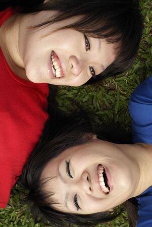 Two happy asian teen girls lying on grass portrait wearing red and blueの写真素材
