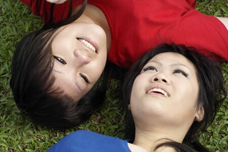 Two happy asian teen girls lying on grass portrait wearing red and blueの写真素材