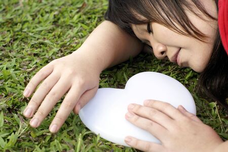 Asian lady sleeping on grass with white heart beside herの写真素材