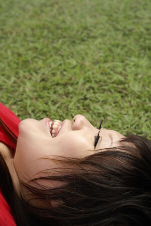 Asian woman in red shirt laughing happily lying on grass portraitの写真素材