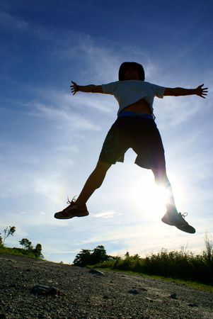 Silhouette of person jumping in air with blue sky and cloudsの写真素材