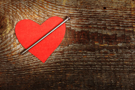 Red cardboard heart with big nail on wooden backgroundの写真素材
