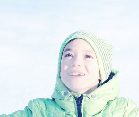 Green hat and jacket clothing boy looking up on snow background. Toned and filtered photoの写真素材