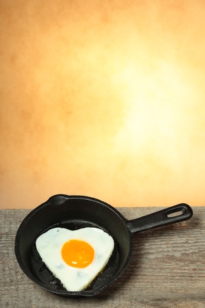 Frying pan with fried egg in shape of heart on old wooden table with abstract backgroundの写真素材