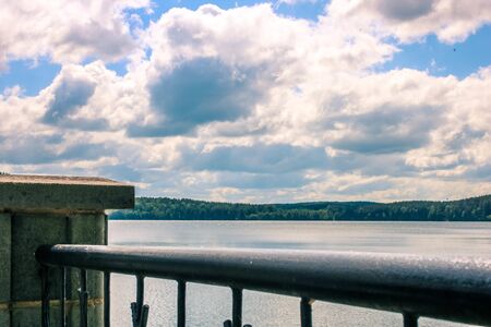 Green forest by the lake under heavy cloudy blue sky view from promenade.の写真素材