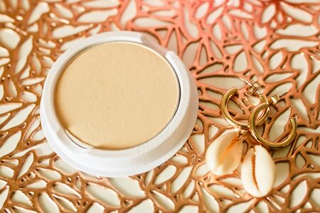 Blusher interchangeable powder cartridges and earrings on golden patterned background.の写真素材