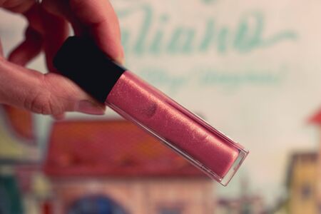Red cream blush lipstick on female hand on colorful blurred background.の写真素材