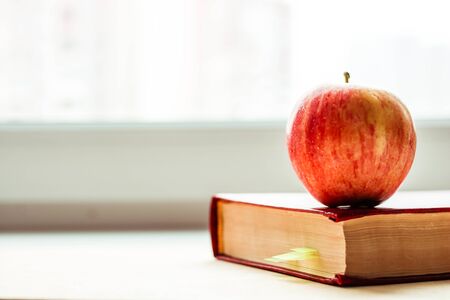 Red book near the window with a red apple on top. Knoweldge apple.