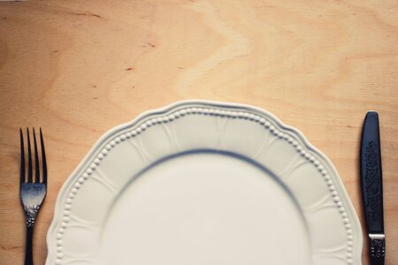 Photo of an empty white plate with knife and fork on a rustic wooden table.
