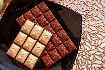 Black plate with pieces of tasty chocolate on golden background, top view. Space for text
