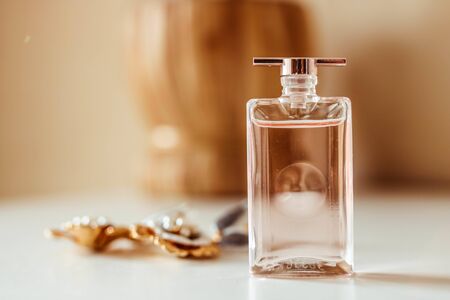 Tasty pink parfume little bottle , in a wide space with golden earrings on blurred background.
