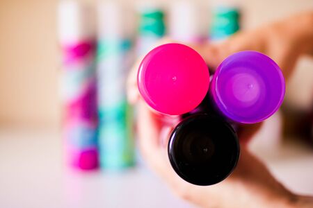 Aerosol cans in female hands. Violet, black and pink caps of deodorant bottles. Abstract blurred background.の写真素材