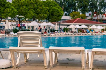 Plastic white plank beds for suntan at hotel standing with umbrellas chaise lounges near the pool.