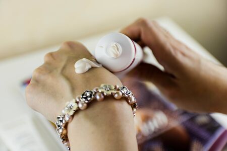 Cropped image of a young woman putting moisturizer onto her hand with very dry skin and deep cracks with cream. Skin care concept.