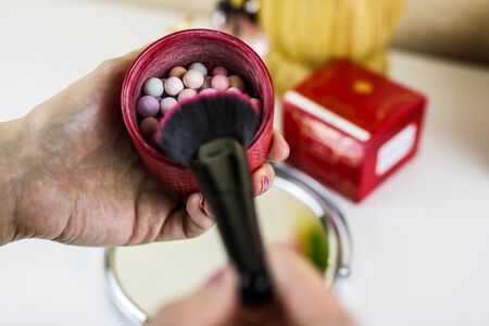 Cosmetic blush in spheres in a hand on a colorful background. Woman getting ready to apply makeup....