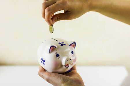 Savings concept. Female hand putting coin into piggy bank on the other hand.の写真素材