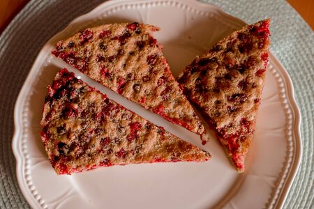 Three baked pieces of homemade cake with berries lie on white plate, wooden table.の写真素材
