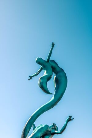 Blue silhouettes of two mermaids against the blue sky.の写真素材
