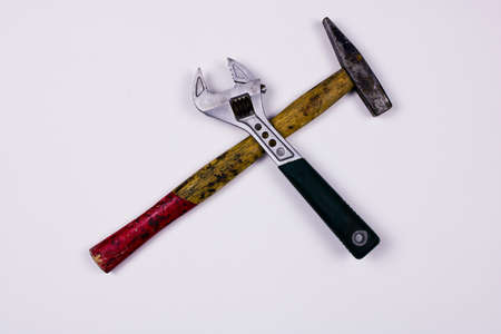 Old adjustable wrench and old hammer form a cross formation on white background. High quality photo