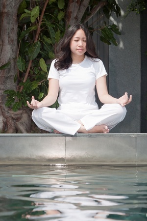 Attractive young asian woman practicing yoga meditation under the tree near the poolの写真素材