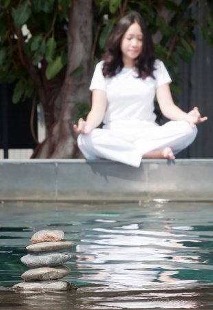 Stack of pebble stones on water with woman practicing yoga meditation in the backgroundの写真素材
