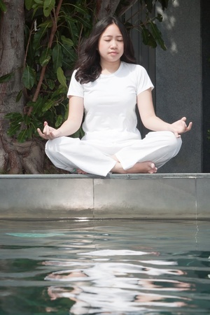 Attractive young asian woman practicing yoga meditation under the tree near the poolの写真素材
