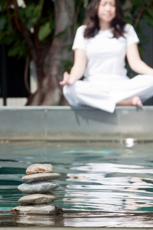 Stack of pebble stones on water with woman practicing yoga meditation in the backgroundの写真素材