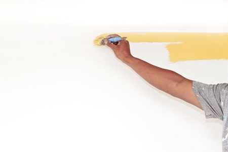 A man's hand painting a wall yellow with paint brushの写真素材