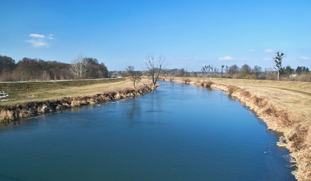 Winter wide river with blue water in open landscape with yellow grass