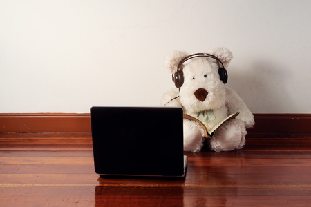 Dog doll in reading book and listening music from the laptop on the wooden floorの写真素材