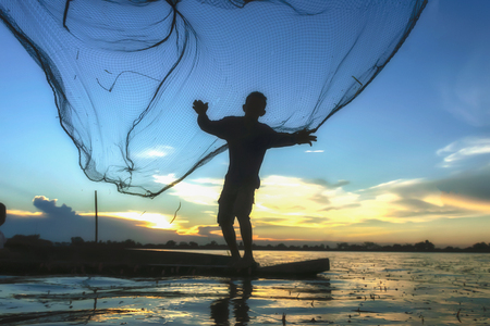 Traditional Asian fishermen throwing net fishing in the river at sunset time.の写真素材