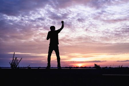 Silhouette of a man with hands raised in the sunset .の写真素材