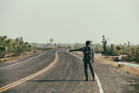 Man hitchhiker standing on a road. Adventure and tourism concept. Vintage filtersの写真素材