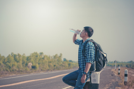 Man hitchhiker standing on a road. Adventure and tourism concept. Vintage filtersの写真素材