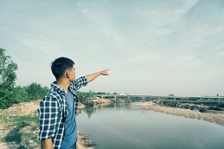 A standing young man on the waterfront pointing  finger  at the sky
の写真素材